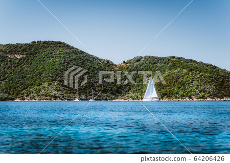 Greece ithaki island, White sail yacht in open blue sea with green island in background 64206426