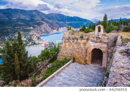 Old fort gate on top of frourio peninsular and Assos village with beautiful sea bay and cypress trees in background. Kefalonia island, Greece Old fort gate on top of frourio peninsular and Assos village with beautiful sea bay and cypress trees in background. Kefalonia island, Greece 64206958