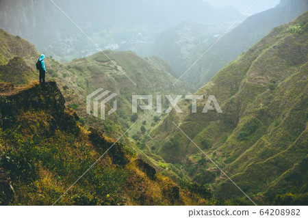 Male hiker on top of the mountain rock with gorgeous panorama view over high mountain ranges and deep valley 64208982