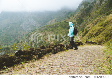 Active vacation tourism. Man enjoying impressive mountainscape. Arid canyon valley extend far below. Santo Antao, Cabo Verde Active vacation tourism. Man enjoying impressive mountainscape. Arid canyon valley extend far below. Santo Antao, Cabo Verde 64209008