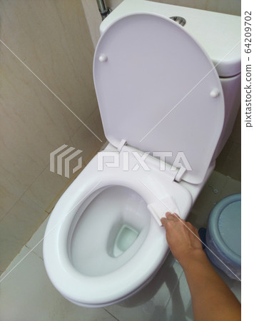 A man's hand uses toilet paper to wipe the toilet lid after the alcohol spray has been disinfected. A man's hand uses toilet paper to wipe the toilet lid after the alcohol spray has been disinfected. 64209702