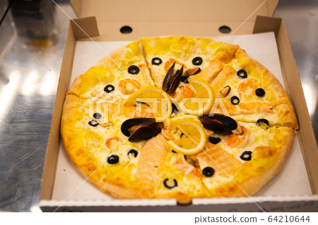 Seafood pizza in a cardboard box on the table Seafood pizza in a cardboard box on the table 64210644