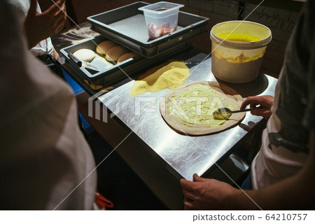 The chef is making pizza. spreads white sauce on The chef is making pizza. spreads white sauce on 64210757
