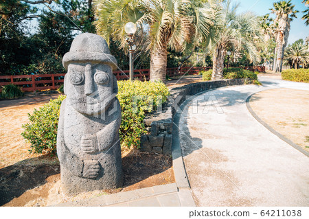 Dol hareubang stone grandpa with tropical palm trees at Daepo Jusangjeolli in Jeju Island, Korea 64211038