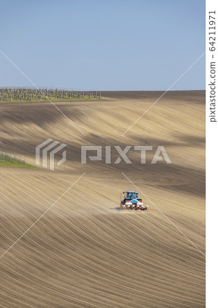 Tractor with seed drill in early spring landscape Tractor with seed drill in early spring landscape 64211971