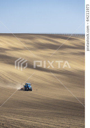 Tractor with seed drill in early spring landscape Tractor with seed drill in early spring landscape 64211973