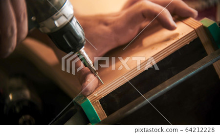 Carpentry working - man worker drills screws into the piece of plywood 64212228