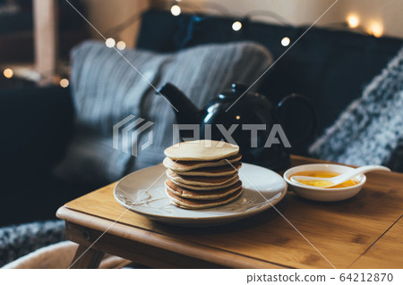 Pancakes with honey on wooden tray in cozy room. Pancakes with honey on wooden tray in cozy room. 64212870