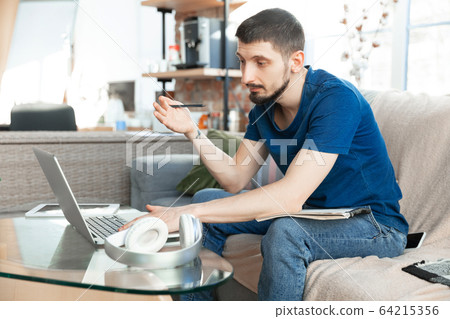 Young focused man studying at home during online courses or free information by hisself Young focused man studying at home during online courses or free information by hisself 64215356