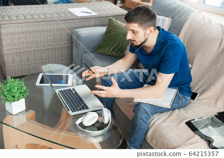 Young focused man studying at home during online courses or free information by hisself Young focused man studying at home during online courses or free information by hisself 64215357