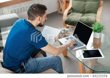 Young focused man studying at home during online courses or free information by hisself Young focused man studying at home during online courses or free information by hisself 64215359
