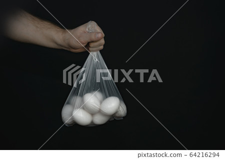 Hand holding plastic bag with white eggs on a Hand holding plastic bag with white eggs on a 64216294