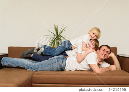 Dad lies on couch and on his back are two 64219396