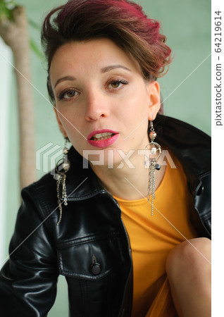 Glam rock style look of a beautiful girl with dark pink hair and mohawk wearing yellow dress and black leather jacket, close-up female portrait 64219614