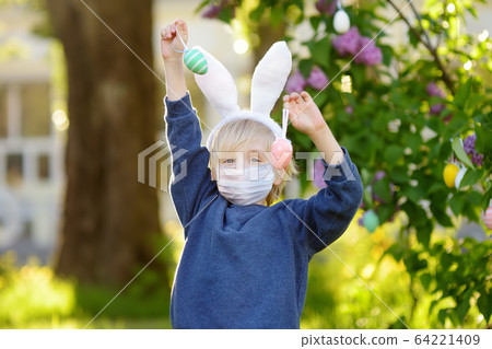 Pretty little boy wearing bunny ears and hunting for eggs in spring park on Easter day Pretty little boy wearing bunny ears and hunting for eggs in spring park on Easter day 64221409
