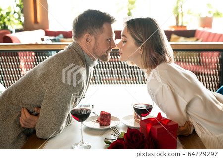 Happy couple bending over table while keeping their faces close to one another Happy couple bending over table while keeping their faces close to one another 64229297
