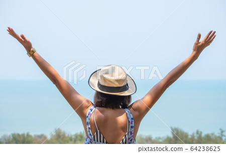 The image behind Asian women raise their arms and wear a hat  background sea. 64238625