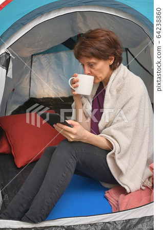Woman sit inside a tent enjoying a cup of tea Woman sit inside a tent enjoying a cup of tea 64238860