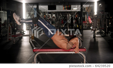 An adult man bodybuilder training his back and stamina in the gym lying on the bench An adult man bodybuilder training his back and stamina in the gym lying on the bench 64239520