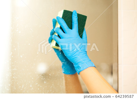 Women hand in a blue rubber glove in the picture, removes and washes bathroom sink by spray and sponge, hygiene concept 64239587