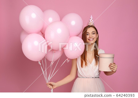 woman in birthday hat celebrating with pastel pink air balloons woman in birthday hat celebrating with pastel pink air balloons 64240393