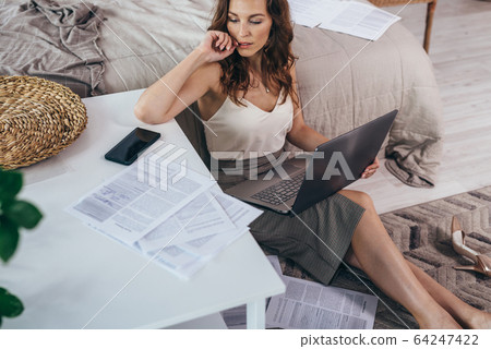 Young woman is sitting on the floor with notebook among documents 64247422