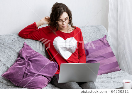 Young girl stay home in quarantine, relaxing on the couch and using the computer. Woman lies on sofa and looks into laptop. Girl resting at home using gadget Young girl stay home in quarantine, relaxing on the couch and using the computer. Woman lies on sofa and looks into laptop. Girl resting at home using gadget 64250211