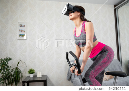 Young girl stay home in quarantine and go in for sports with virtual reality glasses. Woman exercise yoga while at home wearing virtual reality glasses Young girl stay home in quarantine and go in for sports with virtual reality glasses. Woman exercise yoga while at home wearing virtual reality glasses 64250231