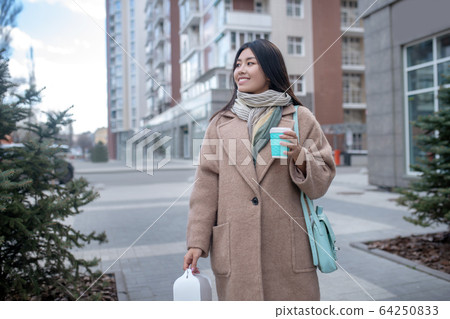 Dark-haired young woman in a beige coat smiling happily 64250833