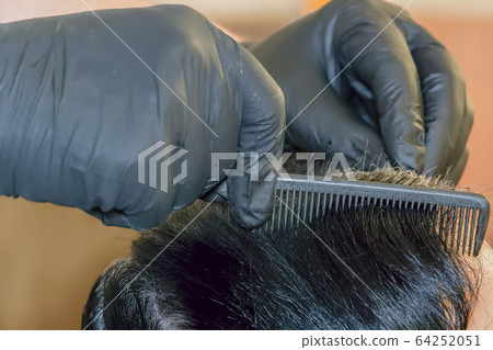 Hair dye color applied on the scalp by a hairdresser wearing black rubber gloves. Hair dye color applied on the scalp by a hairdresser wearing black rubber gloves. 64252051