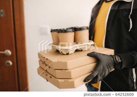 Close up of man hold tree boxes of pizza. Man delivery food and coffe to customer in mask and gloves. Coronavirus theme Close up of man hold tree boxes of pizza. Man delivery food and coffe to customer in mask and gloves. Coronavirus theme 64252600