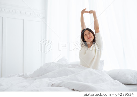 Asian woman wake up in the morning, sitting on white bed and stretching, feeling happy and fresh Asian woman wake up in the morning, sitting on white bed and stretching, feeling happy and fresh 64259534