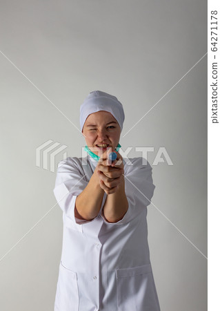 The girl in a medical coat holds a large syringe with blue liquid like a gun 64271178