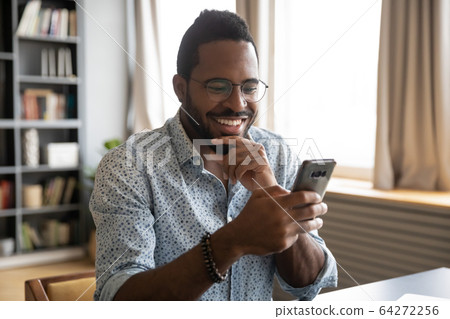 Smiling millennial biracial guy reading pleasant good news sms. Smiling millennial biracial guy reading pleasant good news sms. 64272256