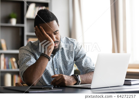 Tired young african man leaning on hand, sleeping at table. 64272257