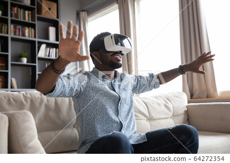 Overjoyed young guy enjoying spending time in virtual reality. Overjoyed young guy enjoying spending time in virtual reality. 64272354