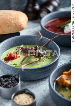 Gray plates with different soups on a gray background. Plate with asparagus soup with octopus, a plate of traditional borscht with sour cream, a plate with mushroom soup and standing on multi-colored 64275934