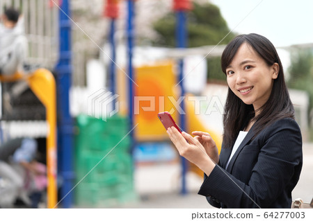 A young lady watching a smartphone in the park 64277003