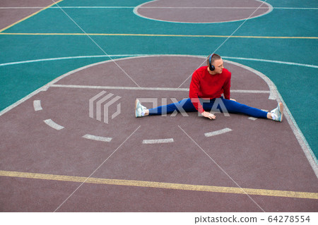 A young man stretches the muscles of his legs after training on the sports ground. 64278554