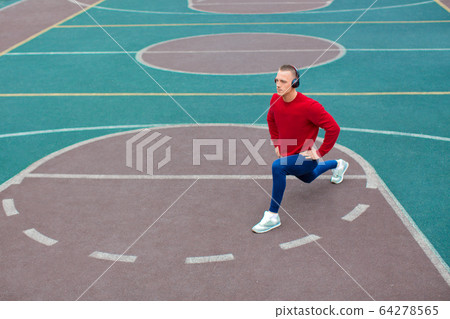 A young man stretches muscles before jogging on the sports ground early in the morning. 64278565