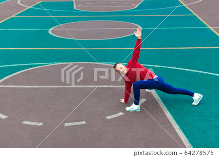 A young man practices yoga on the sports ground early in the morning. 64278575