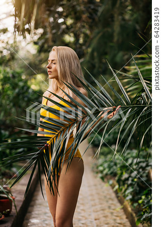 Woman in swimsuit on tropical plants background Woman in swimsuit on tropical plants background 64283419