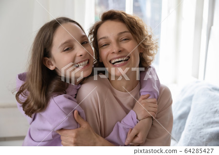 Cheerful affectionate teenage daughter hugging young mom looking at camera 64285427