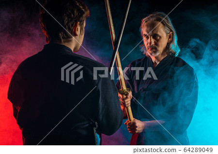 two kendo fighters opposite each other with shinai isolated over dark space 64289049