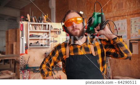 Bearded man worker in yellow shirt standing in the workshop - holding grinding instrument 64290511