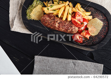 Kebab with french fries, chips and fresh tomatoes, served on a wooden plate. Food photo, traditional Caucasian cuisine. Kebab with french fries, chips and fresh tomatoes, served on a wooden plate. Food photo, traditional Caucasian cuisine. 64290572