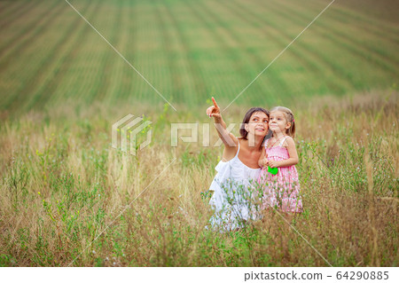 Happy mother and daughter spending time together outdoors, pointing fingers and enthusiastically looking up, with pleasure spending time in countryside 64290885