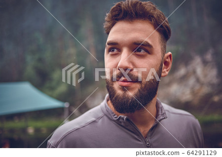 Portrait of a young, bearded man, on, against a background of wildlife. The concept of expedition, adventure and camping life. 64291129