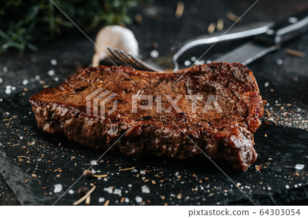 Grilled sirloin steak on the black marble plate seasoned with condiments 64303054