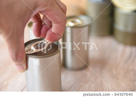 Hand open canned food in metal can on wooden Hand open canned food in metal can on wooden 64307640